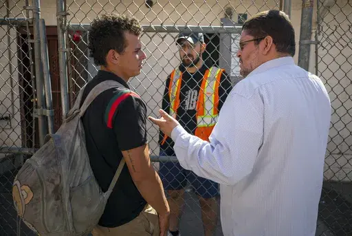 Venezuelan migrant Said Jose, left, asks for help from Jesuit priest Daniel Mora while looking his girlfriend who he got separated with during his detention, at the shelter run by the Sacred Heart Church in El Paso, Texas, Friday, May 12, 2023. The border between the U.S. and Mexico was relatively calm Friday, offering few signs of the chaos that had been feared following a rush by worried migrants to enter the U.S. before the end of pandemic-related immigration restrictions. (AP Photo/Andres Le