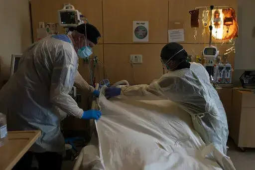 Respiratory therapist Frans Oudenaar, left, and registered nurse Bryan Hofilena cover a body of a COVID-19 patient with a sheet at Providence Holy Cross Medical Center in Los Angeles, Dec. 14, 2021. The fast-moving omicron variant may cause less severe disease on average, but COVID-19 deaths in the U.S. are climbing and modelers forecast 50,000 to 300,000 more Americans could die by the time the wave subsides in mid-March. (AP Photo/Jae C. Hong, File)