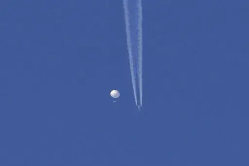 In this photo provided by Brian Branch, a large balloon drifts above the Kingstown, N.C. area, with an airplane and its contrail seen below it. The United States says it is a Chinese spy balloon moving east over America at an altitude of about 60,000 feet (18,600 meters), but China insists the balloon is just an errant civilian airshipused mainly for meteorological research that went off course due to winds and has only limited “self-steering” capabilities. (Brian Branch via AP)