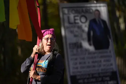 Sheila Eddison protests in front of the home of Leonard Leo during the Mount Desert Island Marathon, Sunday, Oct. 20, 2024, in Northeast Harbor, Maine. (AP Photo/Robert F. Bukaty)