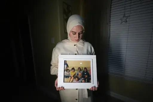 Maryam Kamalmaz hold a photo of her father with some of his 14 grandchildren in Grand Prairie, Texas, Jan. 17, 2024. By any standard, the past 18 months have been remarkable for getting wrongfully detained Americans home. But not so for Kamalmaz, who has had no trace of her father, Majd Kamalmaz, since the psychologist from Texas was stopped at a checkpoint in Syria in 2017 after traveling there to visit an elderly family member. He remains one of several Americans missing in Syria, including jo