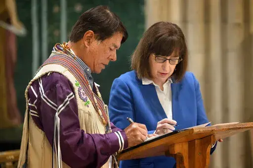 In this image provided by Cornell University, Ray Halbritter, left, representing the Oneida Indian Nation, and Cornell University President Martha E. Pollack, sign documents that repatriate ancestral remains from the university to the Oneida Indian Nation during a ceremony in Sage Chapel, Tuesday, Feb, 21, 2023, in Ithaca, NY. Cornell University has returned ancestral remains to the Oneida Indian Nation that were inadvertently dug up in 1964 and stored for decades in a school archive. (Jason Kos