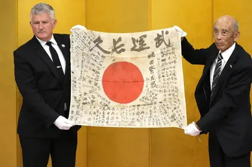 USS Lexington Museum executive director Steve Banta, left, and Toshihiro Mutsuda, the elderly son of Japanese soldier Shigeyoshi Mutsuda, hold together Mutsuda's good luck flag during the handover ceremony of his good luck flag at Yasukuni shrine in Tokyo, Japan, Saturday, July 29, 2023. Mutsuda was only 5 years old when he last saw his father, who was drafted by Japan's Imperial Army in 1943 and killed in action. For him, his father was a bespectacled man in an old family photo standing by a si