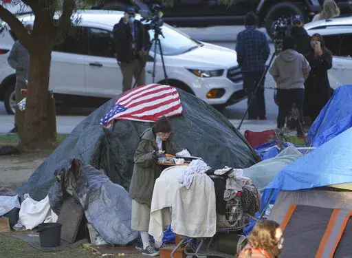 A woman eats at her tent at the Echo Park homeless encampment at Echo Park Lake in Los Angeles, on March 24, 2021. From homelessness to rising crime, Los Angeles residents are unhappy and frustrated. The campaign for the city's next mayor will test if voters in the liberal-minded city could embrace a new mayor with a tough approach to crime and sprawling homeless encampments that have spread into virtually every neighborhood.  (AP Photo/Damian Dovarganes, File)