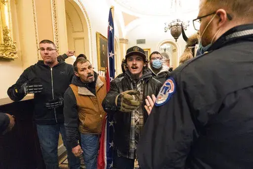 Kevin Seefried, second from left, holds a Confederate battle flag as he and other insurrectionists loyal to President Donald Trump are confronted by U.S. Capitol Police officers outside the Senate Chamber inside the Capitol in Washington, Jan. 6, 2021. A federal judge on Wednesday, June 15, 2022, convicted Kevin Seefried and his adult son Hunter Seefried of charges that they stormed the U.S. Capitol together to obstruct Congress from certifying President Joe Biden’s 2020 electoral victory. (A