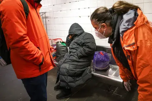 Homeless Outreach personnel reach out to a person sleeping on a bench in the Manhattan subway system, Monday, Feb. 21, 2022, in New York. In New York City's latest effort to address a mental health crisis on its streets and subways, Mayor Eric Adams announced Tuesday, Nov. 29, that authorities would more aggressively intervene to help people in need of treatment, saying there was "a moral obligation" to do so, even if it means providing care to those who don't ask for it. (AP Photo/John Minchill
