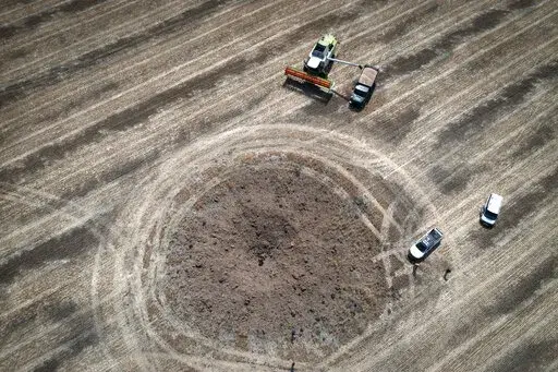 A farmer collects harvest on a field ten kilometres from the front line where fierce battle is going, a crater left by the Russian rocket in the foreground, in the Dnipropetrovsk region, Ukraine, Monday, July 4, 2022. An estimated 22 million tons of grain are blocked in Ukraine, and pressure is growing as the new harvest begins. The country usually delivers about 30% of its grain to Europe, 30% to North Africa and 40% to Asia. But with the ongoing Russian naval blockade of Ukrainian Black Sea po
