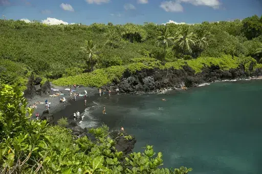 People spend time on the black sand beach at Waianapanapa State Park in Hana, Hawaii, on Sept. 24, 2014. Taking care of Hawaii's unique natural environment costs money and now the state wants tourists to help pay for it, especially because growing numbers are traveling to the islands to enjoy the beauty of its outdoors — including some lured by dramatic vistas they've seen on social media. (AP Photo/Marco Garcia, File)