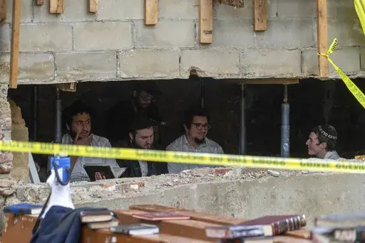 Hasidic Jewish students sit behind a breach in the wall of a synagogue that led to a tunnel dug by the students, Monday, Jan. 8, 2024, in New York. (Bruce Schaff via AP, File)