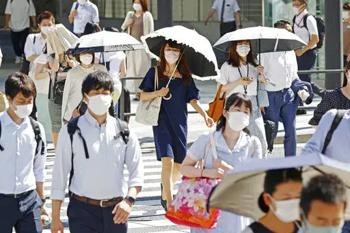 People, some of them holding parasols, cross an intersection amid heat, in Tokyo, Monday, June 27, 2022.  Japan’s government issued a warning for possible power crunch in the Tokyo area Monday, asking offices and residents to save energy as the capital region is hit by sweltering heat, with weather officials announcing an earliest end to the rainy season in decades. (Yusuke Ogata/Kyodo News via AP)