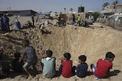 Palestinian children sit at the edge of a crater after an Israeli airstrike in Khan Younis, southern Gaza Strip, Friday, June 21, 2024. (AP Photo /Jehad Alshrafi)