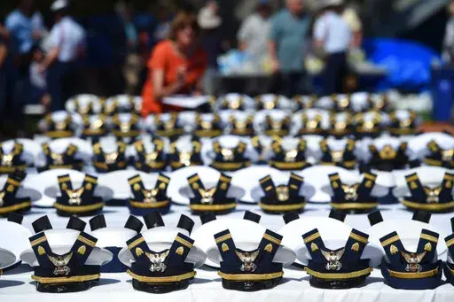 The new hats and shoulder bars for the graduates sit on a table before the start of the U.S. Coast Guard Academy's 141st Commencement Exercises, May 18, 2022, in New London, Conn. A U.S. Coast Guard Academy cadet who was expelled for becoming a father will get his degree as part of a legal settlement, his attorneys said Thursday, Oct. 6, 2022. (AP Photo/Stephen Dunn, File)