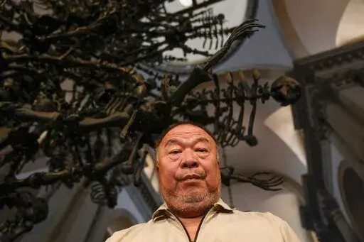 Chinese artist Ai Weiwei poses in front of his unveil glass body of work 'La Commedia Umana' a huge hanging glass sculpture otherwise referred to as a 'chandelier' at the San Giorgio deconsecrated church in Venice, Italy, Friday, Aug. 26, 2022. Chinese artist Ai Weiwei lampoons the surveillance culture and social media with his first ever glass sculpture, made on the Venetian island of Murano, that stands as a warning to the world: "Memento Mori,'' or Latin for "Remember You Must Die." (AP Photo