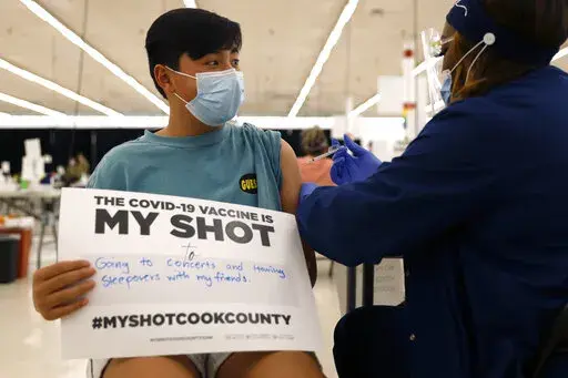 FILE - Lucas Kittikamron-Mora, 13, holds a sign in support of COVID-19 vaccinations as he receives his first Pfizer vaccination at the Cook County Public Health Department, May 13, 2021 in Des Plaines, Ill. The U.S. is expanding COVID-19 boosters as it confronts the omicron surge, with the Food and Drug Administration allowing extra Pfizer shots for children as young as 12. Boosters already are recommended for everyone 16 and older, and federal regulators on Monday, Jan. 3, 2022 decided they’r