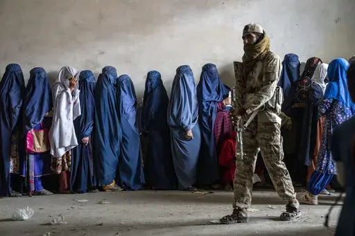 A Taliban fighter stands guard as women wait to receive food rations distributed by a humanitarian aid group, in Kabul, Afghanistan, on May 23, 2023. Human Rights Watch said Monday, Feb. 12, 2024 that Afghanistan’s public health system has been hit hard following a sharp reduction in foreign assistance, coupled with serious Taliban abuses against women and girls, jeopardizing the right to healthcare of millions of Afghans. (AP Photo/Ebrahim Noroozi, File)