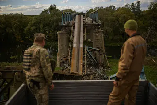 Ukrainian soldiers remove metal structure pieces as they work on a bridge damaged during fighting with Russian troops in Izium, Ukraine, Monday, Oct. 3, 2022. A series of embarrassing military losses for Moscow in recent weeks has presented a growing challenge for prominent hosts of Russian news and political talk shows scrambling to find ways to paint Kyiv's gains in a way that is still favorable to the Kremlin. (AP Photo/Francisco Seco)