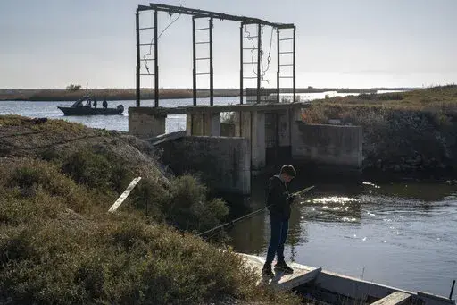 A boy fishes as police border guards on a boat patrol along the Evros River that forms a natural border between Greece and Turkey, on Sunday, Oct. 30, 2022. Greece is planning a major extension of a steel wall along its border with Turkey in 2023, a move that is being applauded by residents in the border area as well as voters more broadly.(AP Photo/Petros Giannakouris)