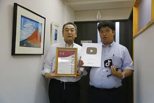 Daikyo Security Chief Executive Daisuke Sakurai, right, and General Manager Tomohiko Kojima hold the awards they have won recently for their Tik Tok videos in the hallway of their Tokyo headquarters office of Daikyo Security Co. in Tokyo Monday, Aug. 22, 2022. They’re your run-of-the-mill Japanese “salarymen,” but the chief executive and general manager at a tiny Japanese security company are among the nation’s biggest TikTok stars, drawing 2.7 million followers and 54 million likes, and