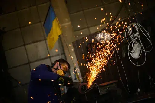 A volunteer shapes metal plates with an angle grinder at a facility producing material for Ukrainian soldiers in Zaporizhzhia, Ukraine, Saturday, May 7, 2022. An old industrial complex in the southeastern Ukrainian riverside city of Zaporizhzhia has become a hive of activity for volunteers producing everything from body armor to camouflage nets, anti-tank obstacles to heating stoves and rifle slings for Ukrainian soldiers fighting the Russian invasion. (AP Photo/Francisco Seco)