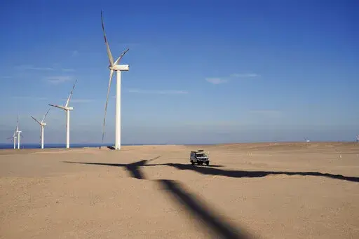 A vehicle drives near wind turbines at Lekela wind power station, near the Red Sea city of Ras Ghareb, some 300 km (186 miles), from Cairo, Egypt, Oct. 12, 2022. The U.N. climate summit is back in Africa after six years and four consecutive Europe-based conferences. The conference — known as COP27 — will be held in the resort city of Sharm el-Sheikh in Egypt. (AP Photo/Amr Nabil, File)
