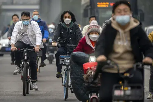 Commuters wearing face masks ride bicycles along a street in the central business district in Beijing, Thursday, Oct. 20, 2022. The World Health Organization downgraded its assessment of the coronavirus pandemic on Friday, May 5, 2023, saying it no longer qualifies as a global emergency. (AP Photo/Mark Schiefelbein, File)
