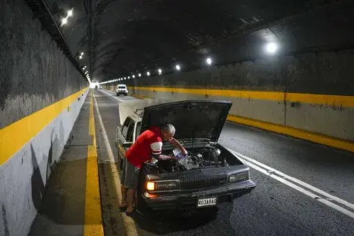 A man tries to cool down his overheating car by pouring water into the radiator, in one of the tunnels of the road that connects La Guaira with Caracas, Venezuela, Tuesday, April 19, 2022. Drivers try to coax a little more life out of aging vehicles in a country whose new car market collapsed and where few can afford to trade up for a better used one. (AP Photo/Matias Delacroix)