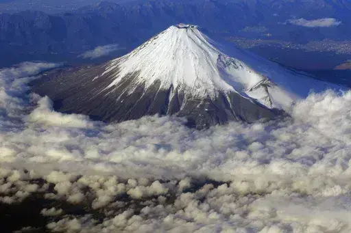 In this Dec. 8, 2010 file photo, snow-covered Mount Fuji, Japan's highest peak at 3,776-meters tall (12,385 feet), is seen from an airplane window. Those who want to climb one of the most popular trails of the iconic Japanese Mount Fuji will now have to reserve ahead and pay a fee as the picturesque stratovolcano struggles with overtourism, littering and those who attempt rushed “bullet climbing,” putting lives at risk. (AP Photo/Itsuo Inouye, File)
