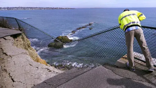 Public Services Director Bill Riccio peers down at debris along the historic Cliff Walk, Tuesday, March 15, 2022, in Newport, R.I. A roughly 30-foot section of the walk crumbled into the sea last week, leaving officials to ponder whether to rebuild or let if continue to fall into the ocean. (AP Photo/Charles Krupa)