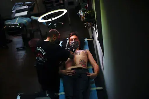 A man, wearing a protective face mask to prevent the spread of coronavirus, is tattooed at Paul and Friends tattoo parlour in downtown Brussels, March 26, 2021. The European Union is imposing restrictions on the inks that tattoo artists can use as of Wednesday, Jan. 5, 2022. The EU says it is a necessary move to protect the health of consumers because thousands of chemical elements now in use can cause anything from allergic reactions to cancer. The tattoo industry complains it is unfairly targe