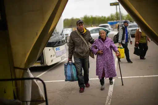 Kateryna Hodza, 85, and her grandson Artem Dorschenko arrive at a reception center for displaced people in Zaporizhzhia, Ukraine, Friday, April 29, 2022. The world is now accustomed to images of millions of Ukrainians on the run from Russia’s invasion. In their shadow are people with a different kind of desperation and daring, heading the other way. (AP Photo/Francisco Seco)