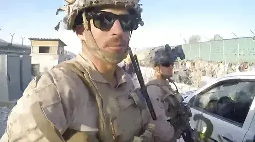 This image from a video released by the Department of Defense shows the explosion, behind he two U.S. Marines in the foreground, by a suicide bomber at Abbey Gate outside Hamid Karzai International Airport on Aug. 26, 2021, in Kabul Afghanistan. The military investigation into the deadly attack during the Afghanistan evacuation has concluded that a suicide bomber, carrying 20 pounds of explosives packed with ball bearings, acted alone, and that the deaths of more than 170 Afghans and 13 U.S. ser