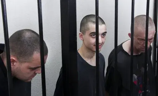 Two British citizens Aiden Aslin, left, and Shaun Pinner, right, and Moroccan Saaudun Brahim, center, sit behind bars in a courtroom in Donetsk, in the territory which is under the Government of the Donetsk People's Republic control, eastern Ukraine, Thursday, June 9, 2022. The two British citizens and a Moroccan have been sentenced to death by pro-Moscow rebels in eastern Ukraine for fighting on Ukraine's side. The three men fought alongside Ukrainian troops and surrendered to Russian forces we