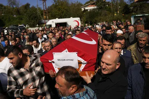 Turkey's Interior Minister Suleyman Soylu, right, helps a coffin covered with a Turkish flag of one of the miners killed in a coal mine explosion, during his funeral in Amasra, in the Black Sea coastal province of Bartin, Turkey, Saturday, Oct. 15, 2022. An official says an explosion inside a coal mine in northern Turkey has trapped dozens of miners. At least 14 have come out alive. The cause of Friday's blast in the town of Amasra in the Black Sea coastal province of Bartin was not immediately 