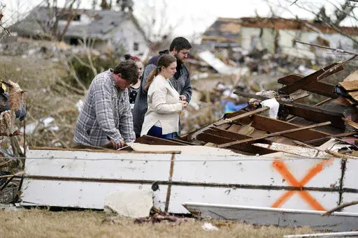 FILE -Brandon Clark, behind, injured from the tornado, returns to his destroyed home for the first time with Laura Shepherd, Tyler Shepherd, left, and his wife Georgialee Clark, behind in the aftermath of tornadoes that tore through the region, in Dawson Springs, Ky., Wednesday, Dec. 15, 2021. One year ago Saturday, Dec. 10, 2022, a massive tornado obliterated wide swaths of Dawson Springs, Ky. (AP Photo/Gerald Herbert, File)