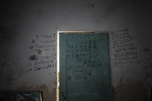 Writing can be seen on a wall and a door in the basement of a school in Yahidne, near Chernihiv, Ukraine, Tuesday, April 12, 2022. Residents say more than 300 people were trapped for weeks by Russian occupiers in  the basement of the school in Yahidne. They wrote the names of people who died during the Russian occupation of their village. (AP Photo/Evgeniy Maloletka)