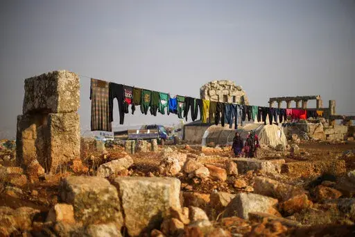 Syrian displaced people walk next to ancient Roman era ruins where they have set their tends in Sarmada district, north of Idlib city, Syria, Thursday, Nov. 25, 2021.  Fallout from the 2-month-old war in Ukraine is worsening long-term humanitarian crises elsewhere, including in Syria.  (AP Photo/Francisco Seco, File)