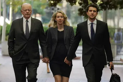 Former Theranos CEO Elizabeth Holmes, center, arrives at federal court with her father, Christian Holmes IV, left, and partner, Billy Evans, in San Jose, Calif., Monday, Oct. 17, 2022. As Elizabeth Holmes prepares to report to prison next week, the criminal case that laid bare the blood-testing scam at the heart of her Theranos startup is entering its final phase. (AP Photo/Jeff Chiu, File)