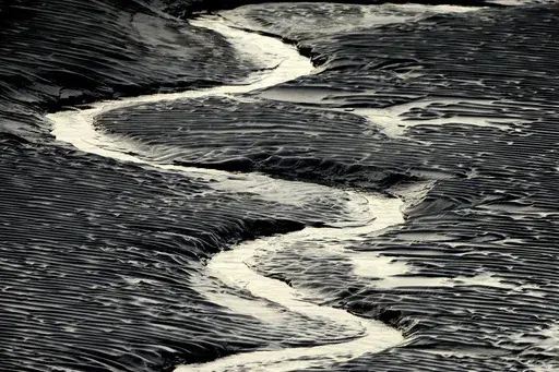 A channel flows through the mud flats along the Seward Highway and Turnagain Arm in Alaska on Oct. 25, 2014. Authorities said, a 20-year-old man from Illinois who was walking Sunday evening, May 21, 2023, on tidal mud flats with friends in an Alaska estuary, got stuck up to his waist in the quicksand-like silt and drowned as the tide came in before frantic rescuers could extract him. (Bob Hallinen/Anchorage Daily News via AP)