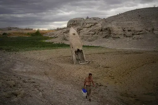 A man walks by a formerly sunken boat standing upright into the air with its stern buried in the mud along the shoreline of Lake Mead amid a drought at the Lake Mead National Recreation Area near Boulder City, Nev., June 22, 2022. Costly weather disasters kept raining down on America last year, pounding the nation with 18 climate extremes that caused at least $1 billion in damage each, totaling more than $165 billion, federal climate scientists calculated Tuesday, Jan. 10, 2023. (AP Photo/John L