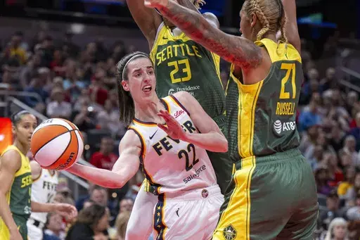 Indiana Fever guard Caitlin Clark (22) passes the ball from under the basket while being defended by Seattle Storm guard Jordan Horston (23) and center Mercedes Russell (21) during the first half of a WNBA basketball game, May 30, 2024, in Indianapolis. Not even a WNBA basketball game is an escape from the arguments and polarization that are so common in American life these days. (AP Photo/Doug McSchooler, File)