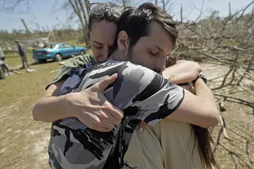 Steve Romero, 23, center, hugs his wife, Hailey Hart, right, and their friend Jessica Soileau, left, after recalling how he, his fiancee and their three dogs rode out Saturday's tornado in their small 1994 Toyota in Tylertown, Miss., on Sunday, March 16, 2024. (AP Photo/Rogelio V. Solis)