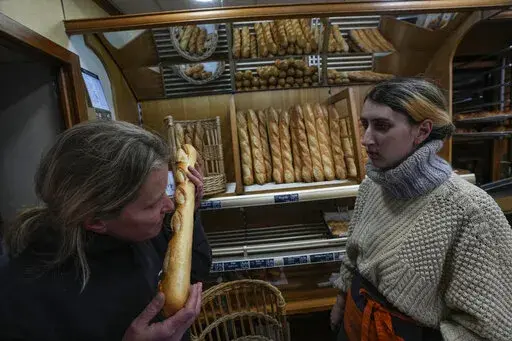 Bakery owner Florence Poirier, LEFT, smells the fresh baguette who comes out of the oven as Mylene Poirier stands next to her at a bakery, in Versailles, west of Paris, Tuesday, Nov. 29, 2022. The humble baguette -- the crunchy ambassador for French baking around the world -- is being added to the U.N.'s list of intangible cultural heritage as a cherished tradition to be preserved by humanity. UNESCO experts gathering Wednesday Nov. 30, 2022 in Morocco decided that the simple French flute deserv