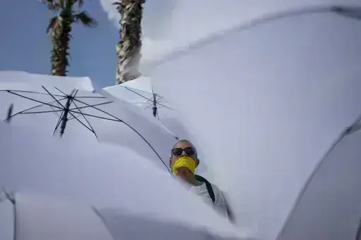 An activist with a yellow ribbon on her mouth holds a white umbrella during a protest calling for the release of hostages held in the Gaza Strip, in front of the U.S. Embassy branch office in Tel Aviv, Israel, Friday, Jan. 31, 2025. (AP Photo/Oded Balilty)