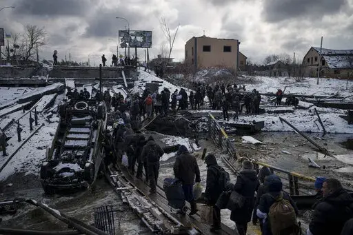 Ukrainians cross an improvised path under a destroyed bridge while fleeing Irpin, in the outskirts of Kyiv, Ukraine, Tuesday, March 8, 2022. As milestones go, the first anniversary of Russia's invasion of Ukraine is both grim and vexing. It marks a full year of killing, destruction, loss and pain felt even beyond the borders of Russia and Ukraine. (AP Photo/Felipe Dana, File)