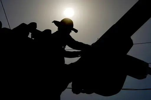 A linesman works on power lines under the morning sun, July 12, 2024, in Phoenix. (AP Photo/Matt York, File)