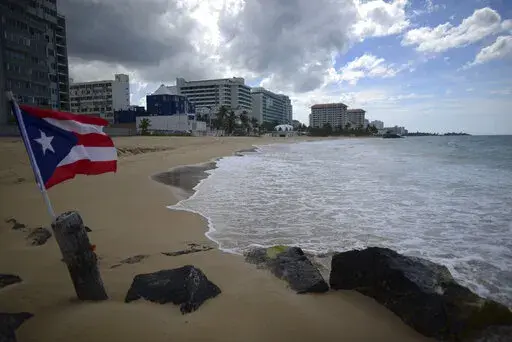 A Puerto Rican flag flies on an empty beach at Ocean Park, in San Juan, Puerto Rico, Thursday, May 21, 2020.  Puerto Rico’s nearly five-year bankruptcy battle was resolved Tuesday, Jan. 18, 2022, after a federal judge signed a plan that slashes the U.S. territory’s public debt load as part of a restructuring and allows the government to start repaying creditors. (AP Photo/Carlos Giusti, File)