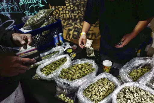 In this April 15, 2019, file photo, a vendor makes change for a marijuana customer at a cannabis marketplace in Los Angeles. An unwelcome trend is emerging in California, as the nation's most populous state enters its fifth year of broad legal marijuana sales. Industry experts say a growing number of license holders are secretly operating in the illegal market — working both sides of the economy to make ends meet. (AP Photo/Richard Vogel, File)