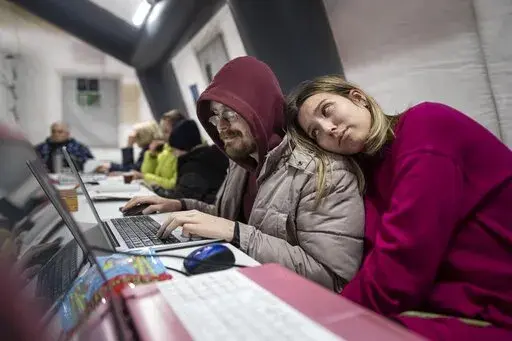 A couple uses a laptop at the heating tent "Point of Invincibly" in Bucha, Ukraine, Monday, Nov. 28, 2022. (AP Photo/Evgeniy Maloletka)