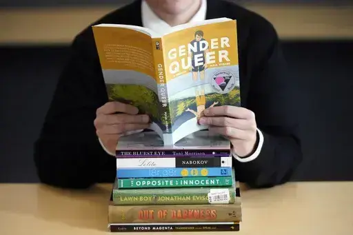 Amanda Darrow, director of youth, family and education programs at the Utah Pride Center, poses with books that have been the subject of complaints from parents on Dec. 16, 2021, in Salt Lake City. With legislators in Florida barring even the mention of being gay in classrooms and similar restrictions being considered in other states, books with LGBTQ+ themes remain the most likely targets of bans or attempted bans at public schools and libraries around the country, according to a new report Mon
