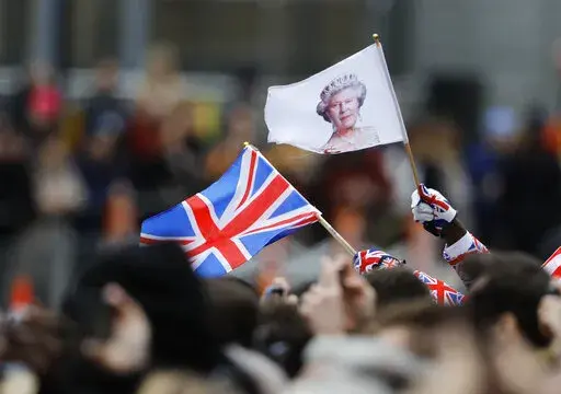 A man waves a British union flag and a flag bearing the image of Britain's Queen Elizabeth II ahead of the annual Commonwealth Day service at Westminster Abbey in London, Monday, March 9, 2020. After seven decades on the throne, Queen Elizabeth II is widely viewed in the U.K. as a rock in turbulent times. But in Britain’s former colonies, many see her as an anchor to an imperial past whose damage still lingers. (AP Photo/Frank Augstein, File)